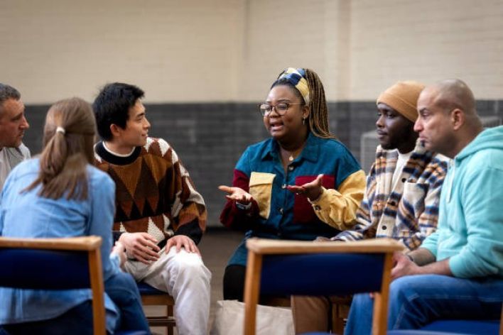 Tormented African American male with dreadlocks sitting on sofa with hands on head during psychotherapy session in cozy room